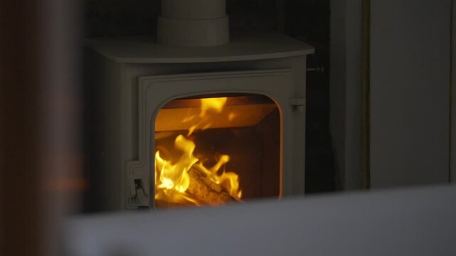 A wood burning stove with a fire in it. The fire is orange and yellow. The stove is in a room with a white wall