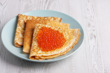 Savory crepes filled with fresh orange fish roe served on a light blue plate at a cozy breakfast table
