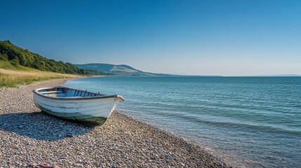 A boat rests on the gravel beach during a sunny summer day. The clear blue sky and distant hills make a beautiful backdrop.