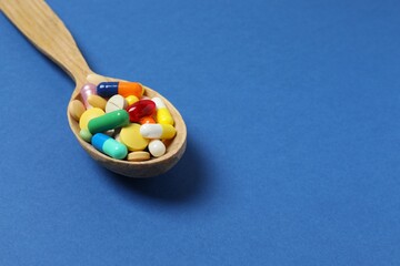 Wooden spoon with pills on blue background, top view