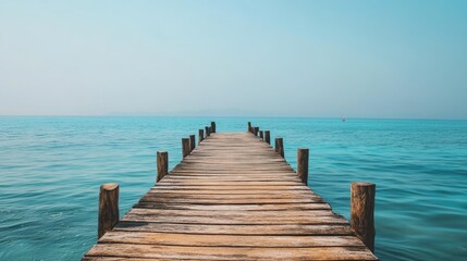 Fototapeta premium A weathered wooden pier reaching out into the ocean, surrounded by the vast blue sea and a clear sky.