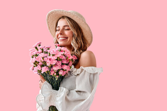 Portrait of a beautiful tender young woman smiling with closed eyes and holding spring pink flowers on a soft pink background. Celebrating International Women's Day.