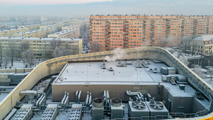 Fototapeta premium winter city landscape from a drone. aerial view of snowy city streets, snowy roofs of buildings on a frosty morning. delicate quiet frosty sunrise over the city. fans and ventilation on the roof
