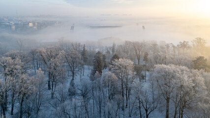 winter city landscape from a drone. fog over the city. aerial view of snowy city streets, snowy roofs of buildings on a frosty morning. delicate quiet frosty sunrise over the city and city park.