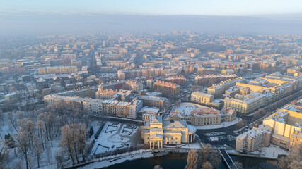 winter city landscape from a drone. fog over the city. aerial view of snowy city streets, snowy roofs of buildings on a frosty morning. delicate quiet frosty sunrise over the city and city park.