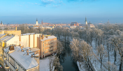 Fototapeta premium winter city landscape aerial view. winter in the city by the river. river dividing the city from the city park. snow-covered roofs of buildings. church towers in the distance