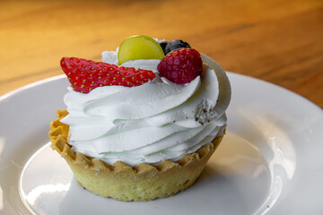 delicious cupcake with fruit and whipped cream on a cake plate. cupcake with strawberries, blueberries, raspberries, grapes. own baking.