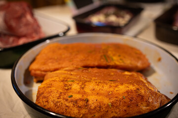 Freshly marinated pork belly coated in a rich spice rub and herbs, placed in a roasting pan, ready for cooking. 