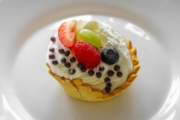a delicious, nicely decorated cupcake with whipped cream and fruit on top. blueberries, strawberries, raspberries, grapes on a homemade muffin.
