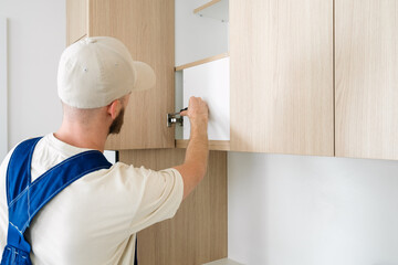Handyman installing shelves in modern wooden kitchen cabinets