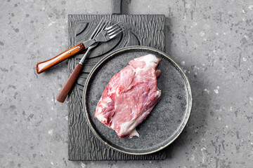 Raw pork steak on a cutting board on a dark background.
