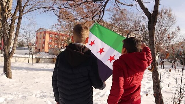 Two children hold and gaze at the Syrian Revolution Flag with bright hope for a better future for themselves and all Syrians in exile, dreaming of returning to their homeland, in a snowy atmosphere.