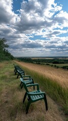 Empty chairs lined up along a grassy hill overlook vast fields and a cloudy blue sky during the late afternoon