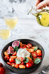 burrata ball with cherry tomatoes, basil leaves, figs and olive oil in a bowl on the table.