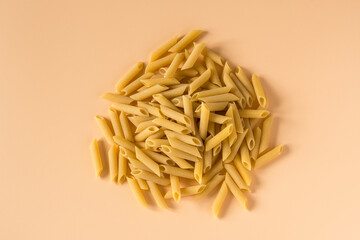 Top view of a raw italian durum wheat penne lisce pasta against a light ochre background . Raw dry...
