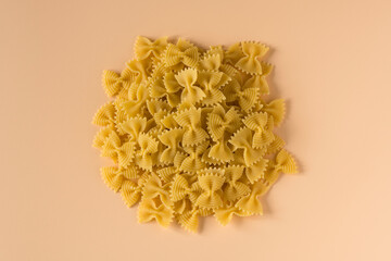 Top view isolated of a raw italian durum wheat farfalle pasta against a light ochre background .