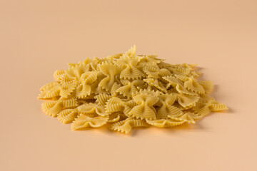 Side view isolated of a raw italian durum wheat farfalle pasta against a light ochre background .