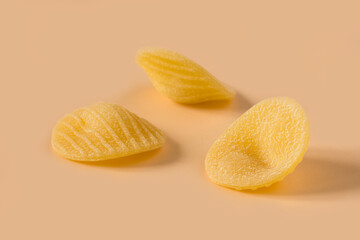 Orecchiette pasta isolated on light ochre background , top view . Macro shot of three isolated raw...
