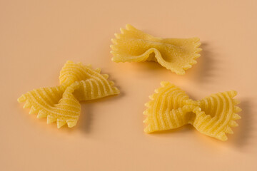 Farfalle, butterfly pasta isolated on light ochre background , side view . Macro shot of three...