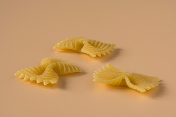 Farfalle, butterfly pasta isolated on light ochre background , side view . Macro shot of three...