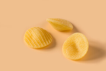 Orecchiette pasta isolated on light ochre background , side view . Macro shot of three isolated raw...