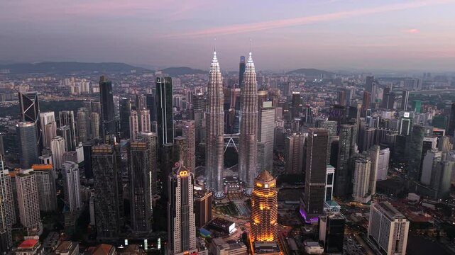 Kuala Lumpur skyline near KLCC drone video. Aerial view of Petronas Towers with pink glow from sky at dusk.