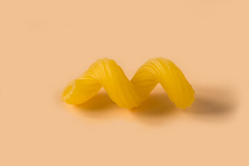 Cavatappi pasta isolated on light ochre background , top view . Macro shot of one isolated raw...