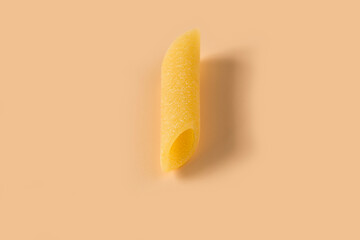 Penne lisce pasta isolated on light ochre background , top view . Macro shot of one isolated raw...