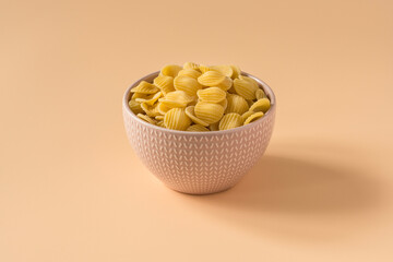 Side view of a bowl of isolated raw italian durum wheat orecchiette pasta against a light ochre...