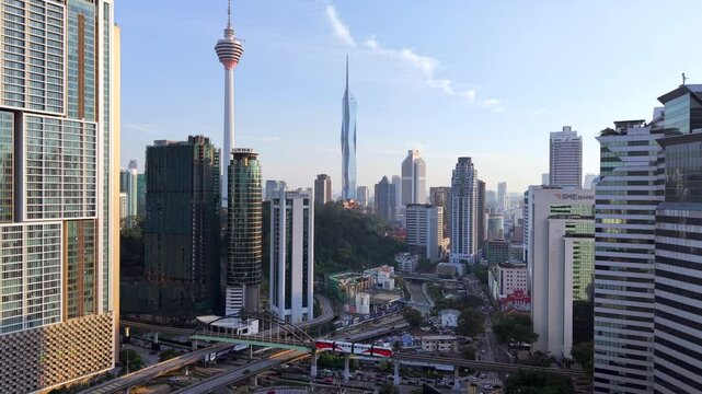 Traffic and light rail train in Kuala Lumpur. Aerial drone video Malaysian capital city near Chow Kit with various modes of transportation in foreground. KL Tower and Merdeka 118 in background.