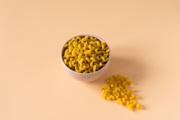 Top  view of a porcelain bowl of raw italian durum wheat cavatappi pasta against a light ochre...