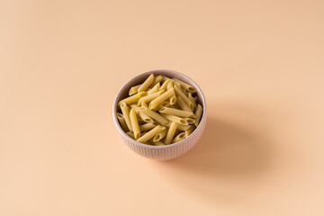 Top view of a bowl of raw italian durum wheat penne lisce pasta against a light ochre background ....