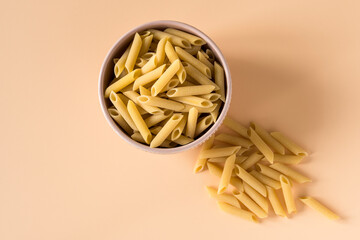 Top view of a bowl of raw italian durum wheat penne lisce pasta against a light ochre background ....
