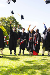 Graduating diverse students tossing caps in air, celebrating in garden with joy, copy space