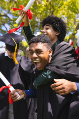 In school, graduating diverse students holding diplomas and cheering joyfully in garden