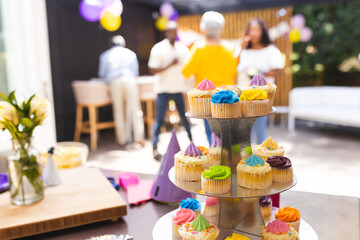 Cupcakes on display at diverse family gathering, people celebrating in background