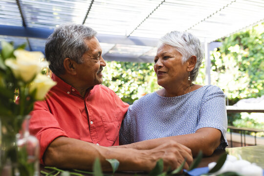 Smiling senior diverse couple sitting together at in garden cafe, enjoying conversation - Powered by Adobe