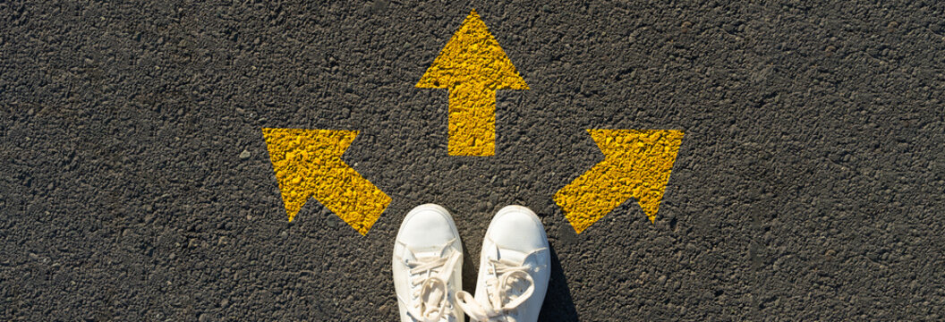 Image from above, girl's boots and arrows on the asphalt, concept of making a choice