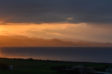 Golden sunset illuminates distant mountains over tranquil sea landscape in vibrant evening sky