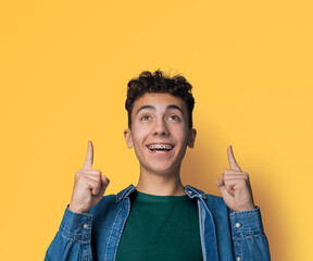 Black curly hair man in braces, open mouth, wear blue denim shirt, green t-shirt advertise point...
