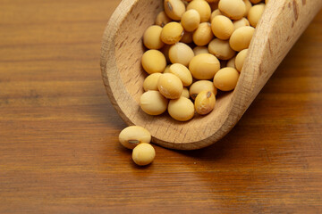 Close em uma concha de madeira com grãos de soja sobre uma mesa de madeira.