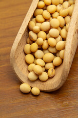 Close em uma concha de madeira com grãos de soja sobre uma mesa de madeira.