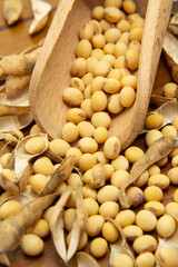 Close de uma concha de madeira cheia de grãos de soja e vários feijões espalhados sobre uma mesa de madeira.