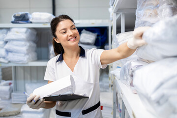 Portrait of female laundry worker standing in dry cleaning service storage room. In background,...