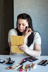 Vertical image of Millennial Caucasian woman doing self make up applying powder with make up brush...