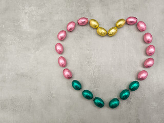 Chocolate easter eggs forming a heart shape on a gray background copy space