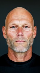 Obraz premium Portrait of a middle-aged bald man with a serious expression against a dark background.