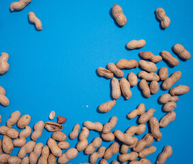 Scattered peanuts on a blue background with broken shells and nuts exposed.Copy space for text.