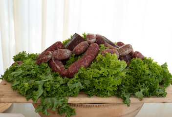 Rustic display of artisanal salami on a bed of fresh green curly kale. The natural lighting highlights the texture and color contrast, perfect for culinary and traditional food photography