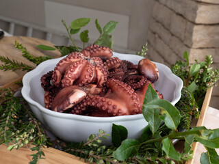 Fresh cooked octopus served in a white ceramic bowl, garnished with fresh herbs against a rustic backdrop. Mediterranean seafood styling with natural lighting and organic elements